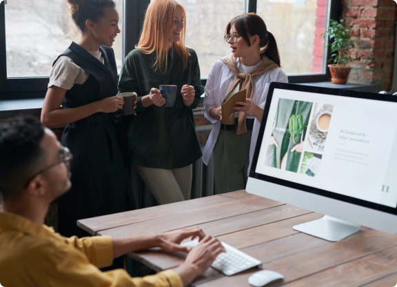 Парень за компьютером и три девушки разговаривают рядом