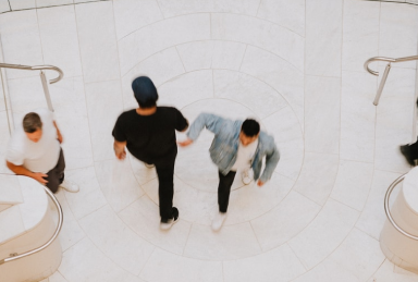 в помещении с белой плиткой на полу два мужчины проходят мимо друг друга в противоположные стороны