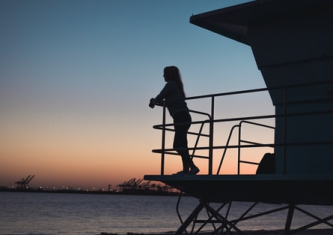 черный силует женщины, которая стоит на балконе и смотрит на восход солнца над морем